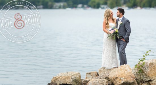 Bride and groom on rocks on shores of Lake Winnipesaukee, New Hampshire